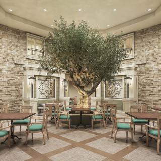 An indoor dining area featuring a large tree surrounded by tables and chairs, with stone walls adding to the ambiance.