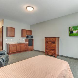 A minimalist studio apartment featuring a bed, kitchenette, and wooden furniture.