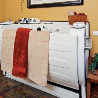 An accessible bathtub with towels hanging over the side in a warmly decorated bathroom.