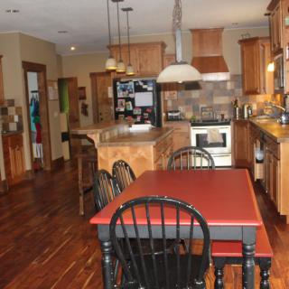 A cozy kitchen with wooden cabinets, a red dining table, and overhead lighting.