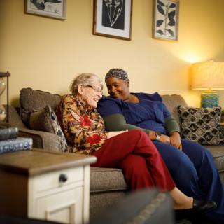 Two people share a warm conversation on the couch in a cozy living room setting.