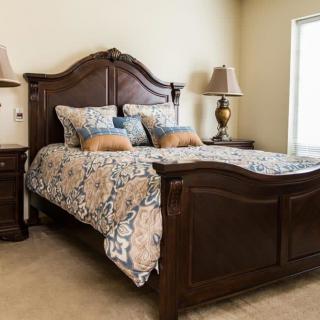A cozy bedroom with a wooden bed frame and matching nightstands, adorned with elegant bedding and decorative pillows.
