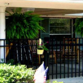 A cozy porch with rocking chairs and lush ferns hanging above, surrounded by a black fence.