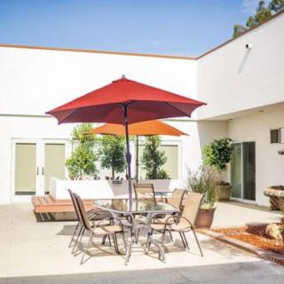 A sunny courtyard with a patio table and chairs set under a red umbrella.