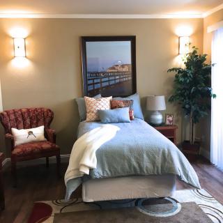 A cozy bedroom with a single bed, upholstered armchair, wall lamps, and decorative plants.