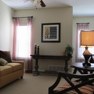A cozy living room with a sofa, elegant table, and soft lighting, accentuated by curtains framing the windows.