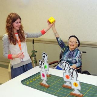 An elderly person in a wheelchair celebrating with a young woman while playing a game indoors.