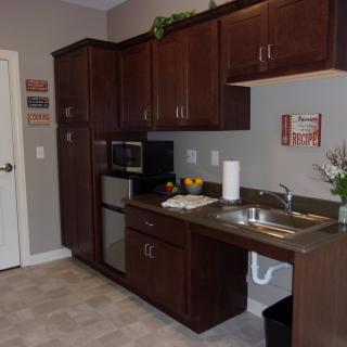 A compact kitchen area featuring dark wood cabinets, a microwave, and a small sink.