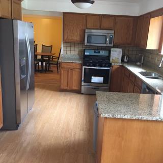 A modern kitchen with wood cabinets and granite countertops, featuring stainless steel appliances and a view into the dining room.