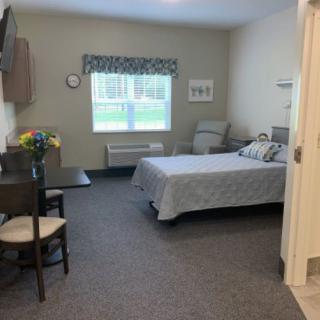 A well-lit bedroom with a neatly made bed, a table and chair placed near a window allowing natural light to fill the room.