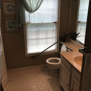 A well-lit bathroom featuring a toilet, sink, and large windows with curtains.