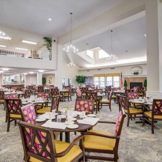 A spacious restaurant dining room with neatly arranged tables and chairs, illuminated by ceiling lights.