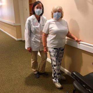A healthcare professional assists a patient during rehabilitation in a facility, both wearing masks for protection.