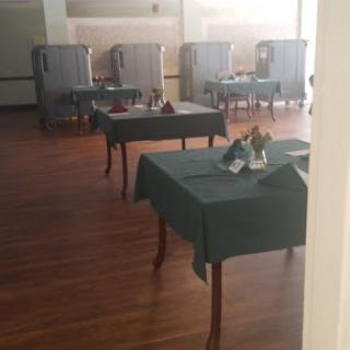 An empty dining area set with green tablecloths, featuring neatly arranged tables and wooden flooring.