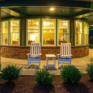 A cozy front porch with two rocking chairs and a small table, warmly lit during the evening.