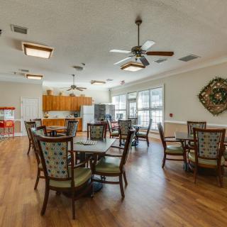 Spacious dining area with multiple tables and chairs, featuring ceiling fans and a kitchen area.