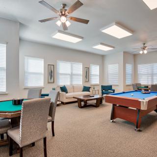 A spacious game room featuring a pool table, seating area, and ceiling fans.