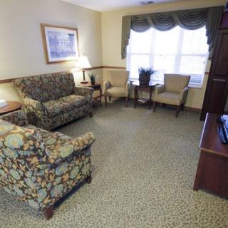 A cozy living room with patterned sofas, chairs, and a coffee table arranged around a carpet.