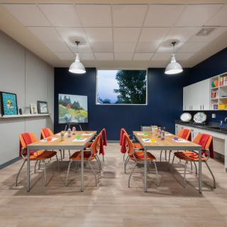 A well-organized classroom with tables and chairs, equipped with art supplies and decorated with posters.
