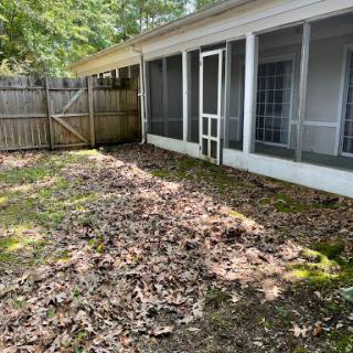 A serene backyard area with fallen leaves and a fenced-off screened porch.