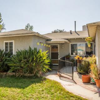 A single-story house with a front yard adorned with plants on a sunny day.