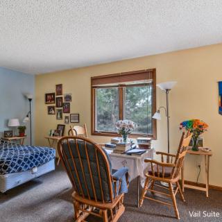 A cozy bedroom with a bed, desk, and chairs by the window, decorated with photos and flowers.
