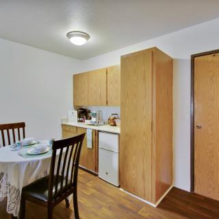 A cozy kitchen and dining area with wooden cabinets, a round table set for a meal, and warm wood flooring.