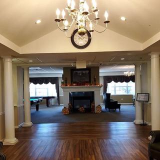 A spacious lobby featuring a chandelier, fireplace, and elegant wooden flooring, framed by decorative columns.