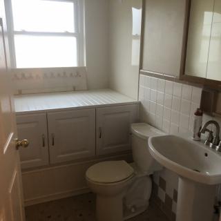 A compact bathroom featuring a sink, toilet, and built-in cabinets under a window.