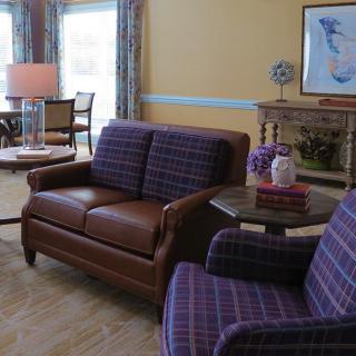 A cozy living room with a brown sofa and purple plaid chairs, featuring a fireplace and tasteful decor.