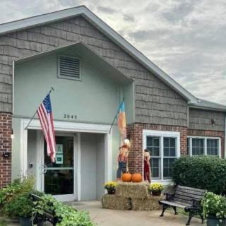 A building entrance adorned with fall decorations and flags, featuring a bench and pumpkins.