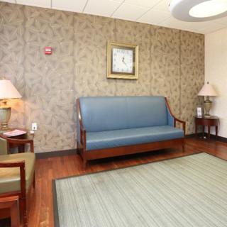 A comfortable waiting area featuring a sofa, chairs, lamps, and a decorative rug.