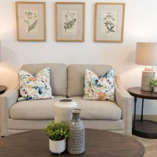 A cozy living room with a neutral sofa, floral cushions, and botanical artwork on the wall.