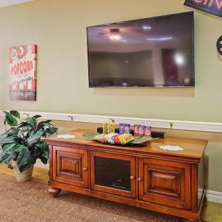 A cozy living room setup featuring a large television mounted on the wall above a wooden cabinet, complemented by decorative plants and wall art.