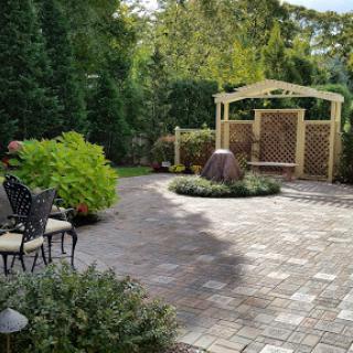 A serene outdoor garden space featuring a patio with chairs, lush greenery, and a decorative lattice archway.