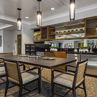 A modern dining area with a large table and chairs, featuring stylish lighting and kitchen amenities.