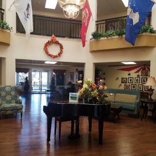 A spacious lobby featuring a grand piano, decorative wreath, flags, and elegant lighting.