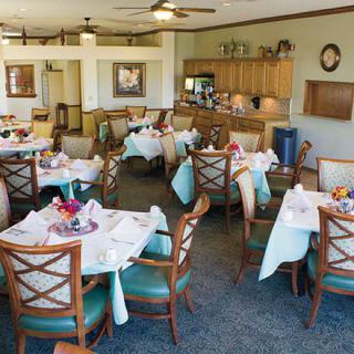 A cozy dining area with neatly arranged tables and chairs, accompanied by a kitchen space.