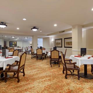 A spacious dining room with elegantly set tables and chairs, featuring warm lighting and decorative artwork on the walls.