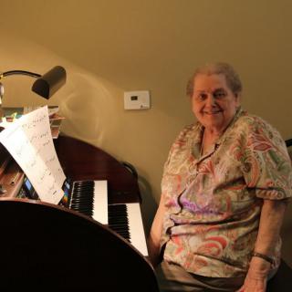 An elderly woman sitting at a piano with sheet music.
