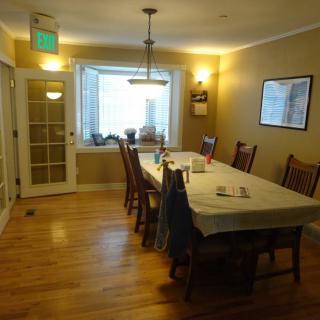 A cozy dining room featuring a long table with chairs, wooden flooring, and warm lighting.