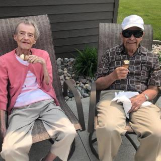 An elderly couple enjoying ice cream while sitting outdoors.