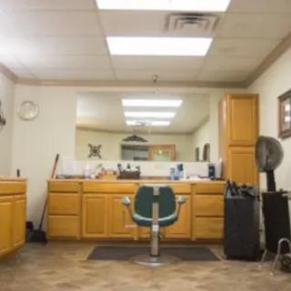 An empty barbershop interior featuring a central chair, mirrors, and wooden cabinets.