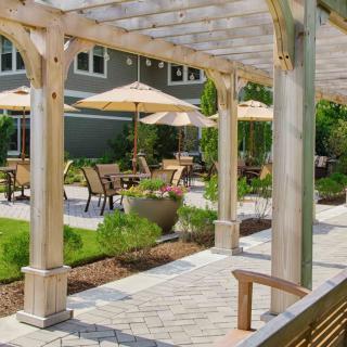 A beautifully landscaped patio area with a pergola, tables, chairs, and umbrellas.