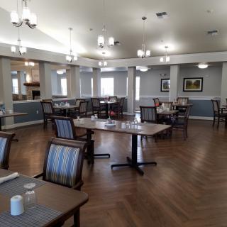 An empty dining area with neatly arranged tables and chairs, featuring elegant lighting and wooden flooring.
