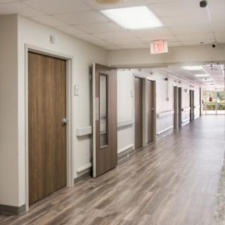 A view of a well-lit hospital hallway featuring wooden doors and modern flooring.