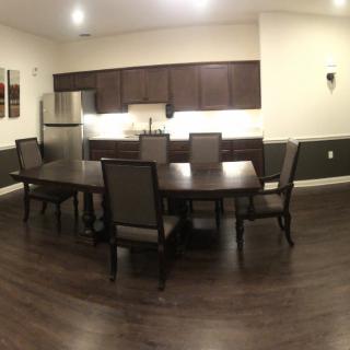 A modern dining area adjacent to a kitchen, featuring a wooden dining table and chairs, with surrounding cabinets and appliances.