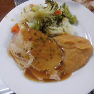 A hearty dinner plate featuring sliced meat with gravy, accompanied by mashed potatoes and a mix of steamed vegetables.