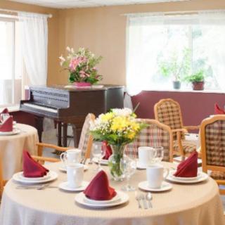 A warmly lit dining area featuring elegantly set tables with red napkins and a piano in the background.