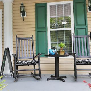 A cozy front porch with two black rocking chairs and a small table decorated with a potted plant.